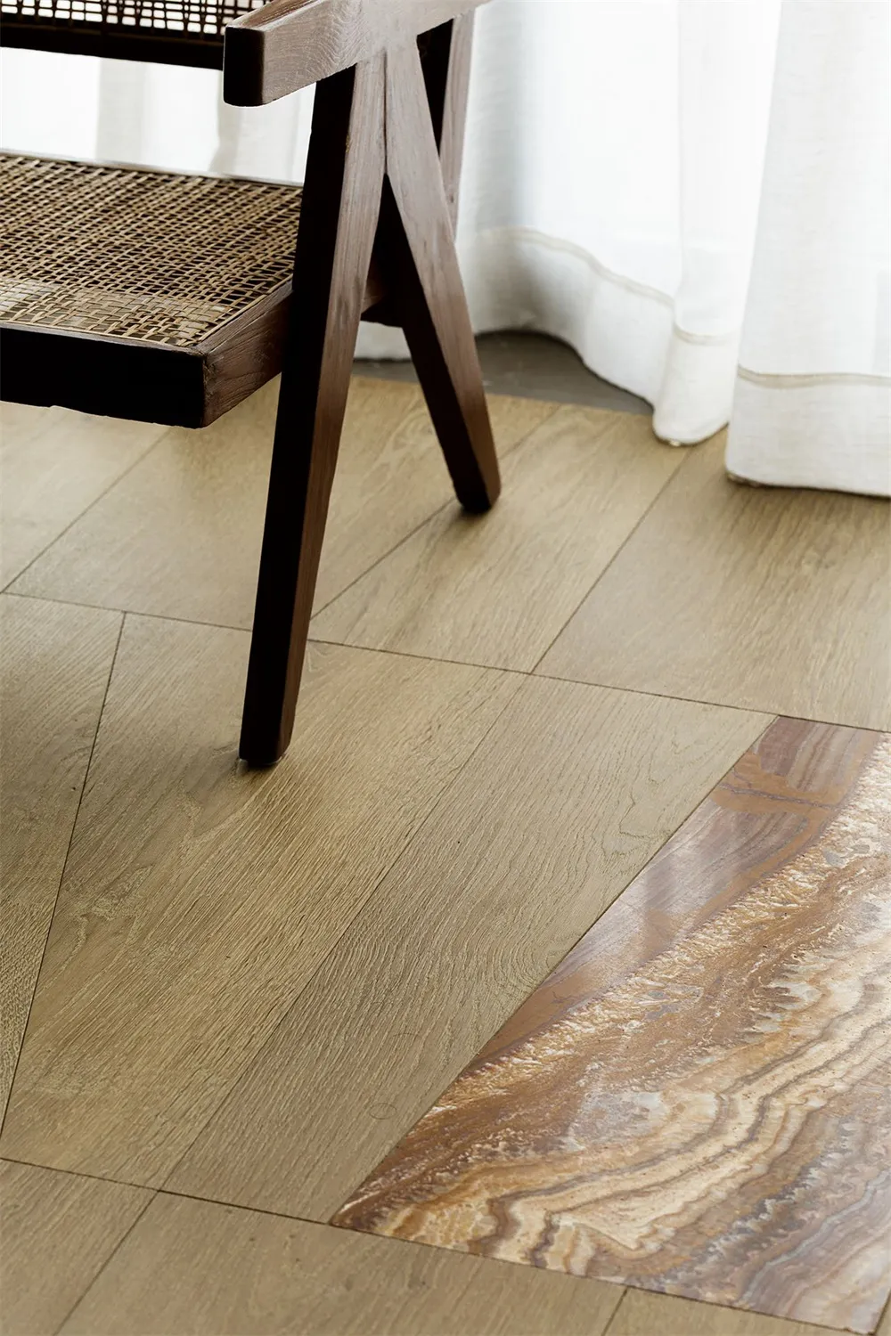 A modern interior featuring a solid wooden floor with a woven rattan chair and white curtains.