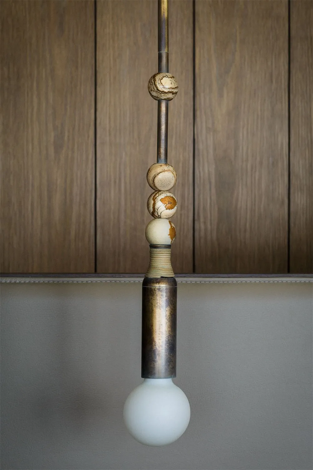 Modern minimalist lighting fixture with marble and leather elements hanging against a grey background.