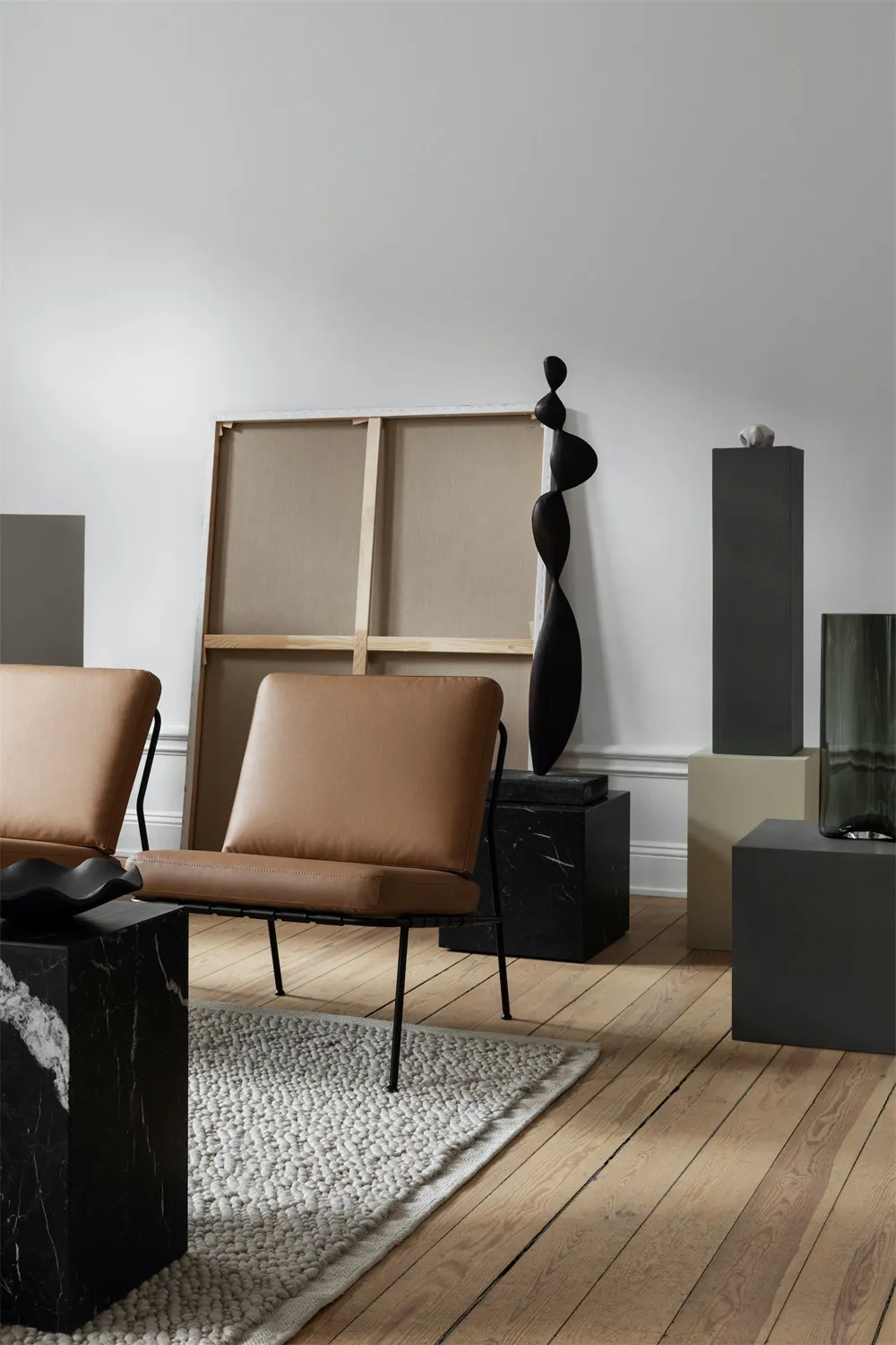A modern living room featuring minimalist furniture, a minimalist art piece, and a gray rug on a wooden floor.