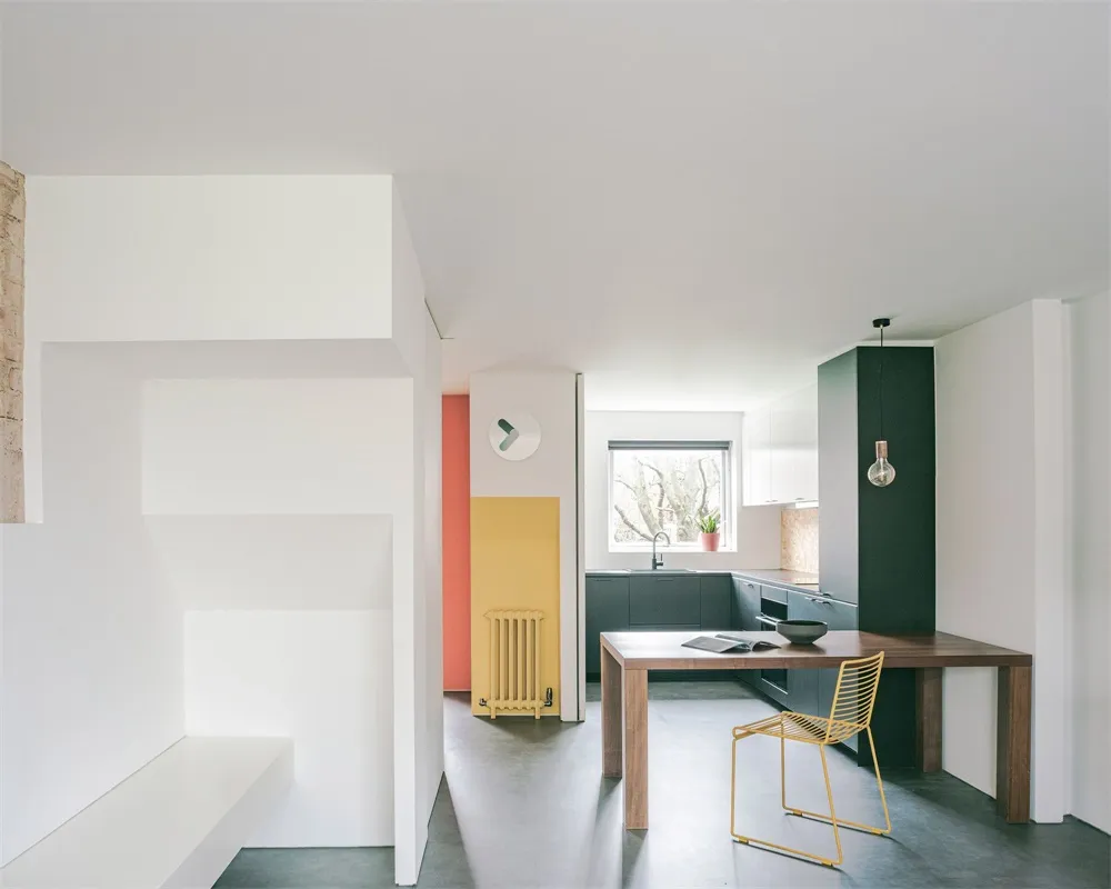 Modern minimalist residential kitchen with white walls, a wooden dining table, and a yellow radiator.