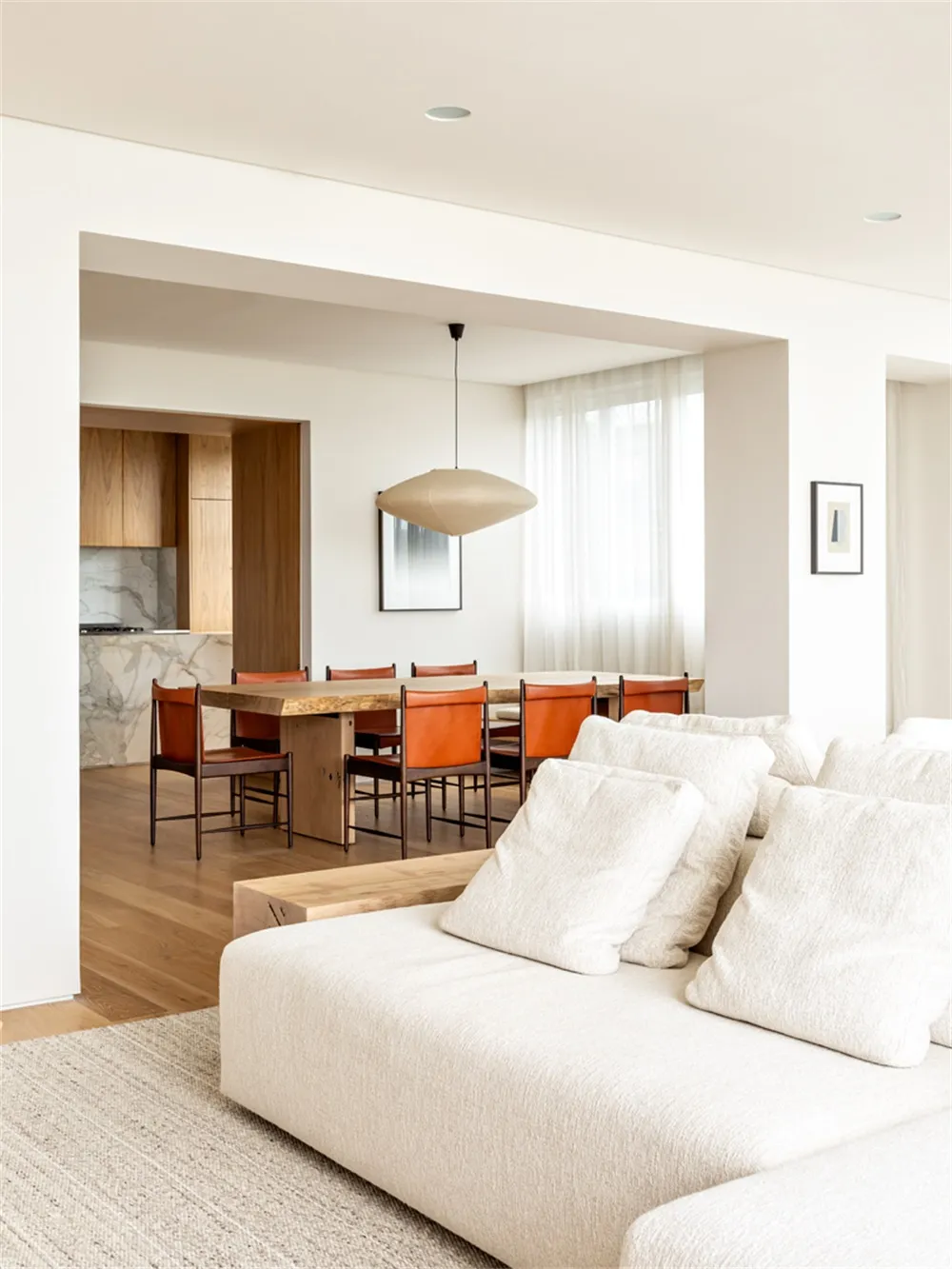 A minimalist living room with a white sofa, wooden dining table, and leather chairs.