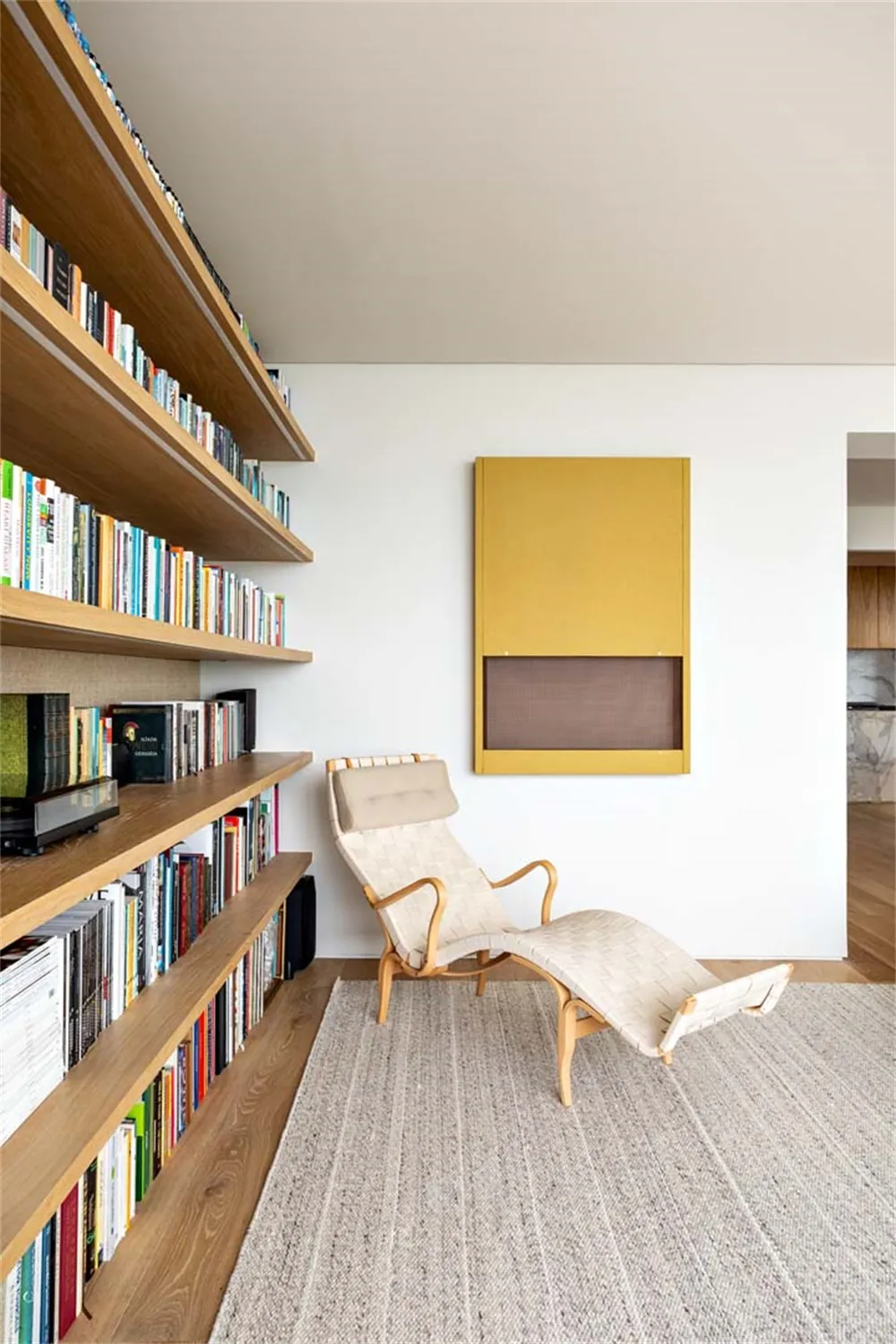 Modern living room featuring a large bookshelf with books, a white lounge chair, and a yellow and brown modern artwork on the