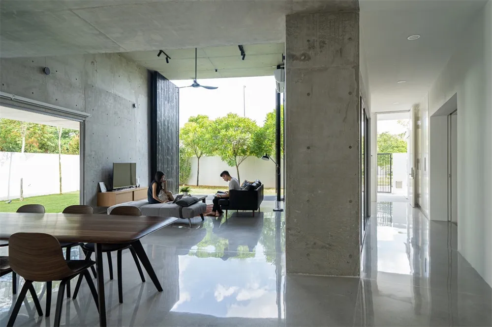 A modern living room with concrete walls, a dining area, and a view of the garden.