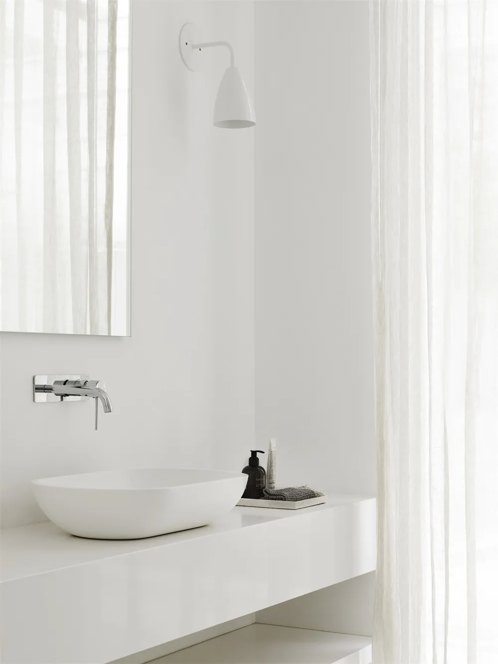 Modern minimalist bathroom featuring a white porcelain ceramic sink and countertop against a white wall and floor.