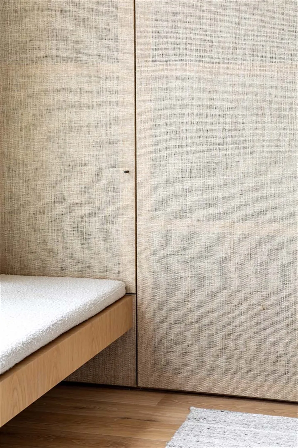 A minimalist bedroom featuring a bed with a wooden frame, backrest cushion, and wooden flooring.