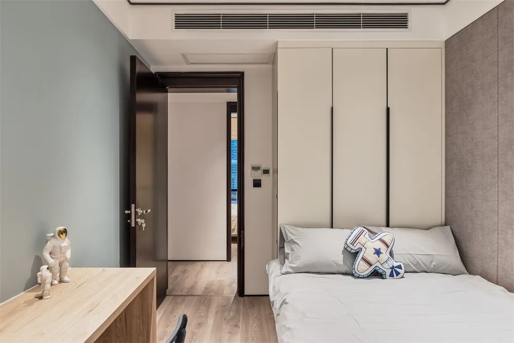 A modern bedroom featuring a wooden desk, upholstered bed with a decorative pillow, and metal accents.