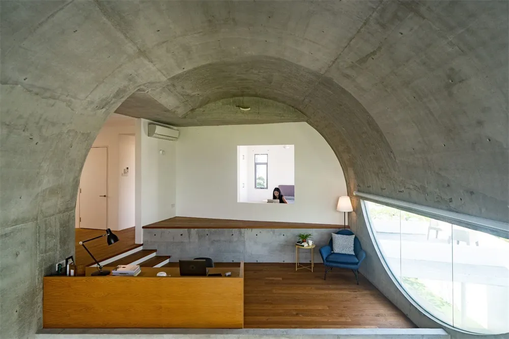 A modern industrial living room with concrete walls, wooden furniture, and large windows.