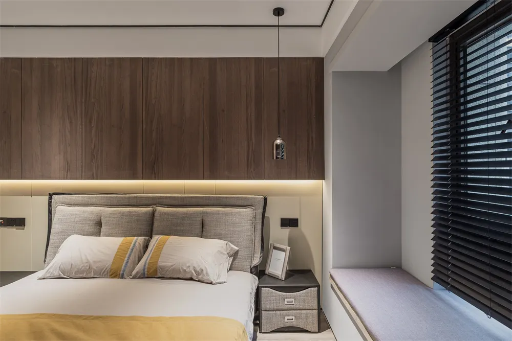 Modern minimalist bedroom featuring a wooden bed frame, white sheets, and gray headboard with a nightstand and bench.