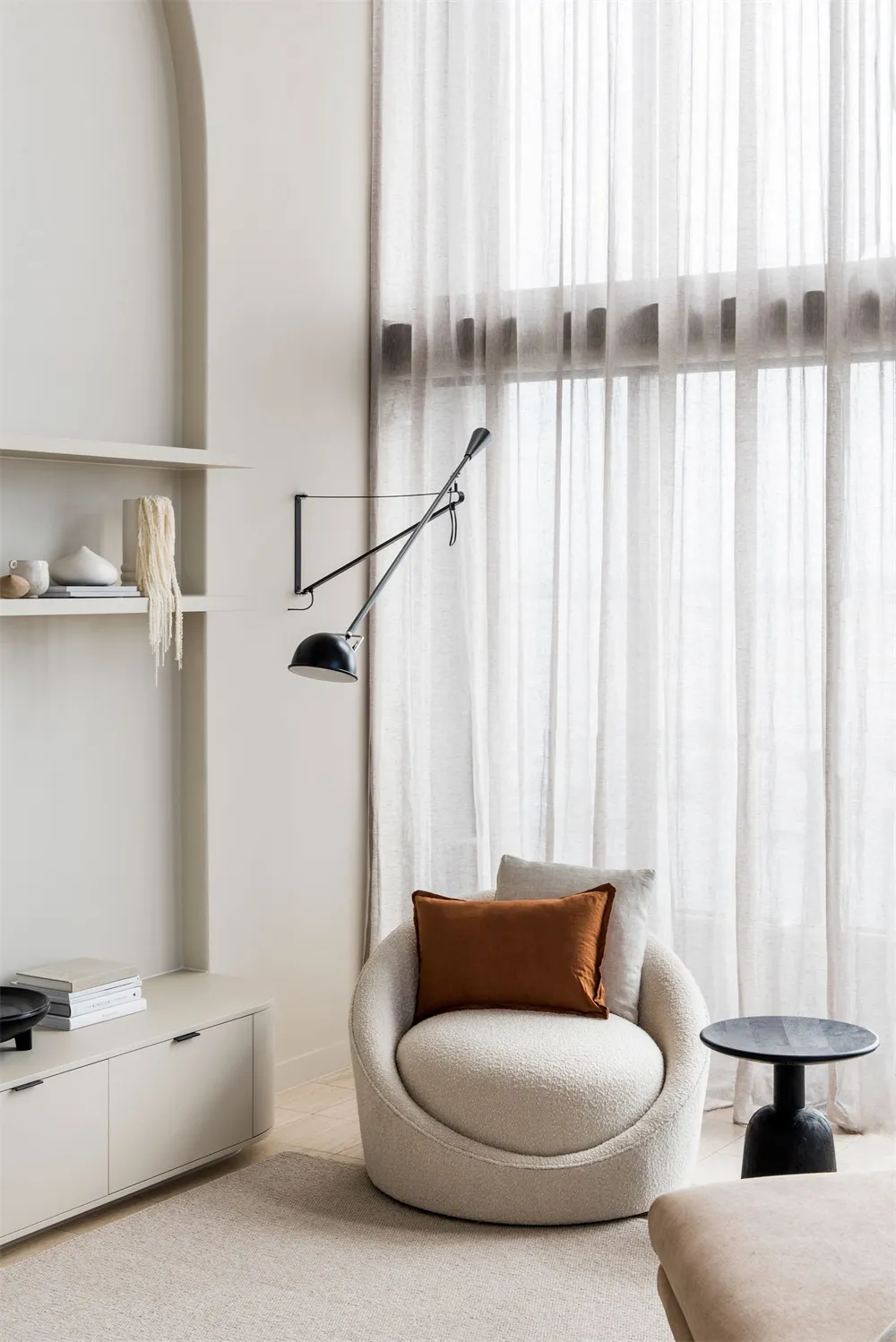 A minimalist living room with white curtains, a sleek armchair, and a minimalist lamp.