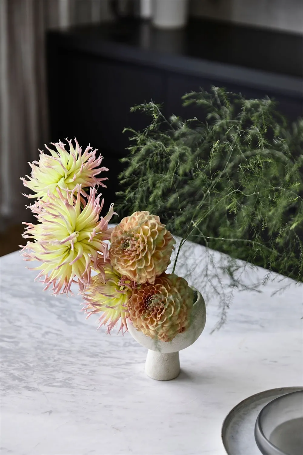 a bouquet of delicate flowers arranged in a modern vase, placed on a marble surface.