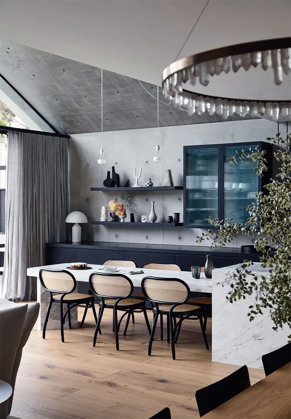 A modern dining room featuring a table, chairs, and decorative shelving against a concrete wall.