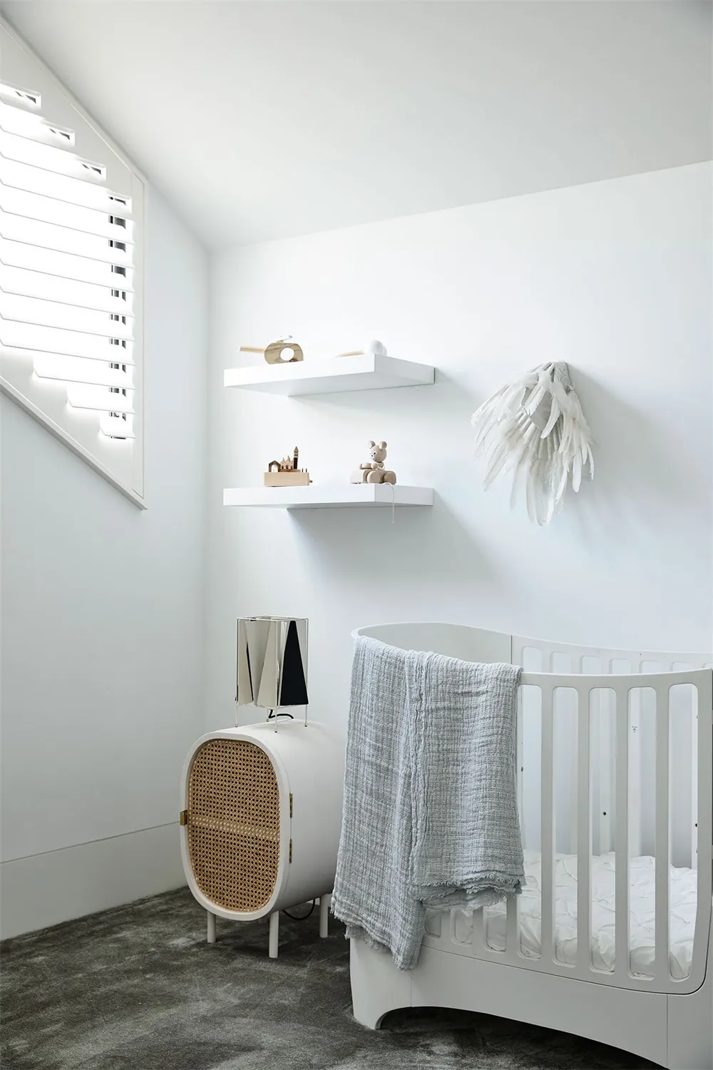A white nursery with a crib, shelves, and a white bed adorned with towels.