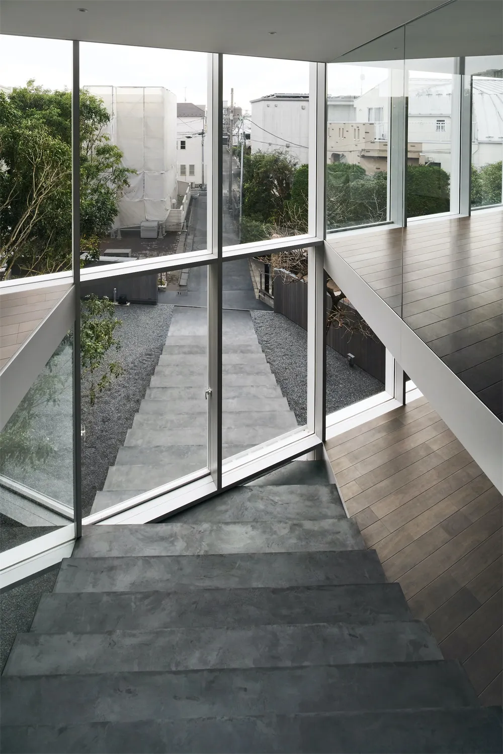 A modern staircase with glass walls and wooden flooring leading to an outdoor area.
