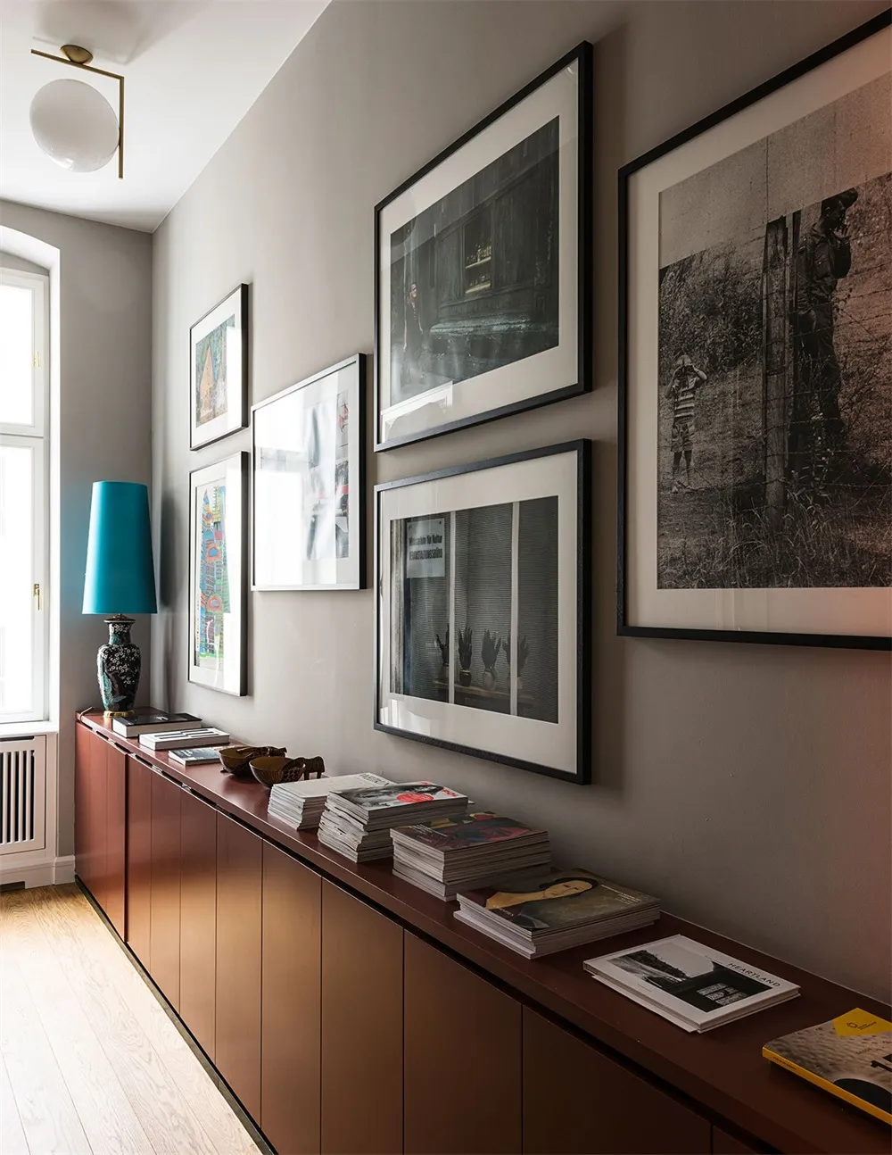 A modern interior entryway featuring wooden cabinets, framed photographs on the wall, and a teal lamp.