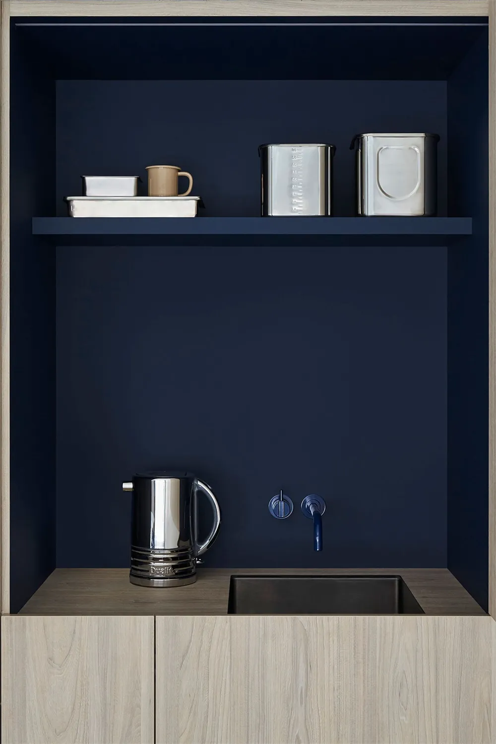 A modern kitchenette featuring metal shelves and a sink with a water dispenser.