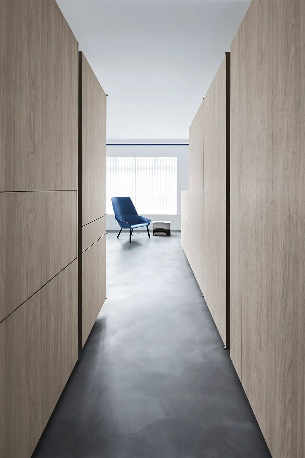 Modern minimalist office space with wooden finishes, blue chair, and large window.