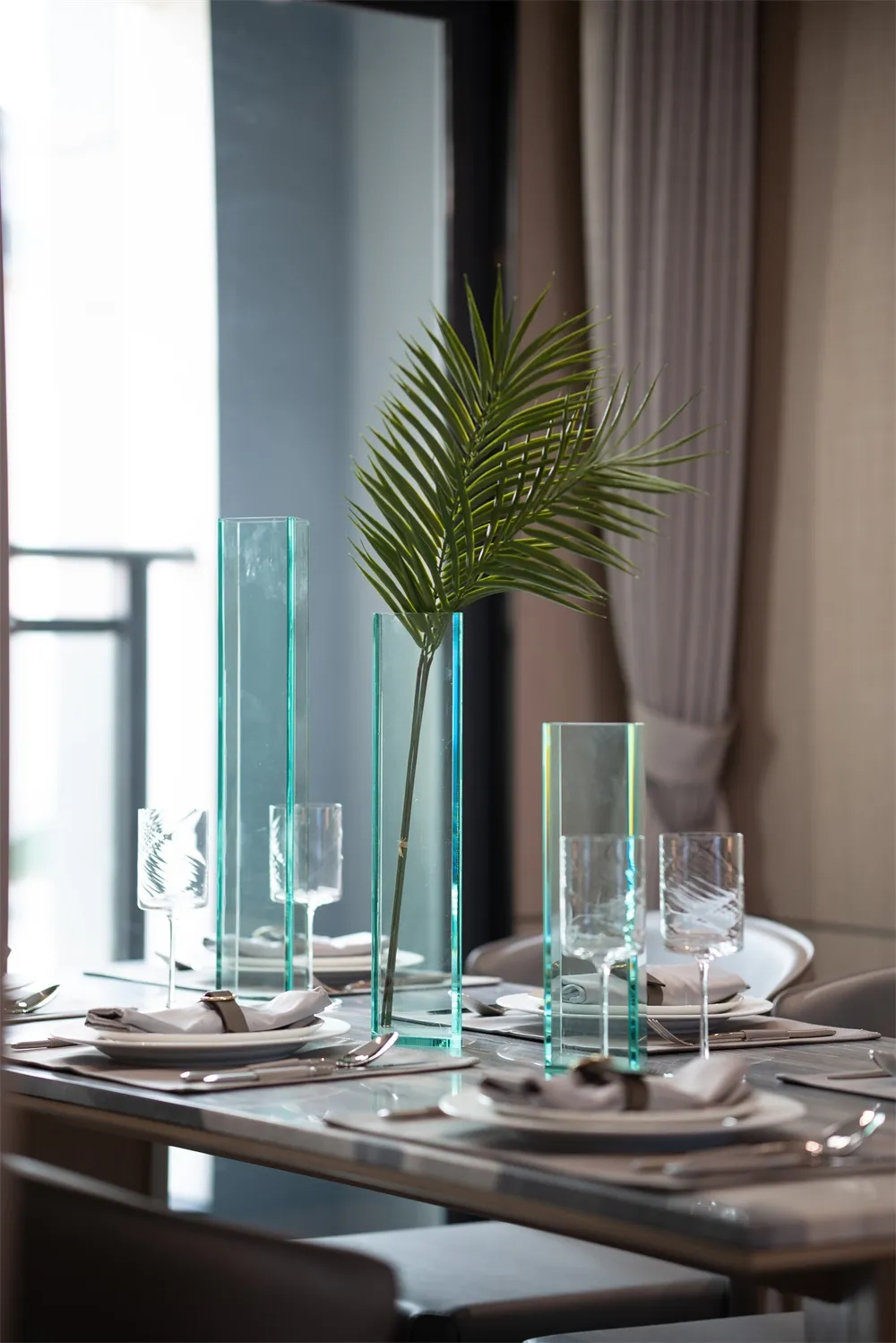 Modern table setting featuring glass vases and a green plant centerpiece on a dining table.