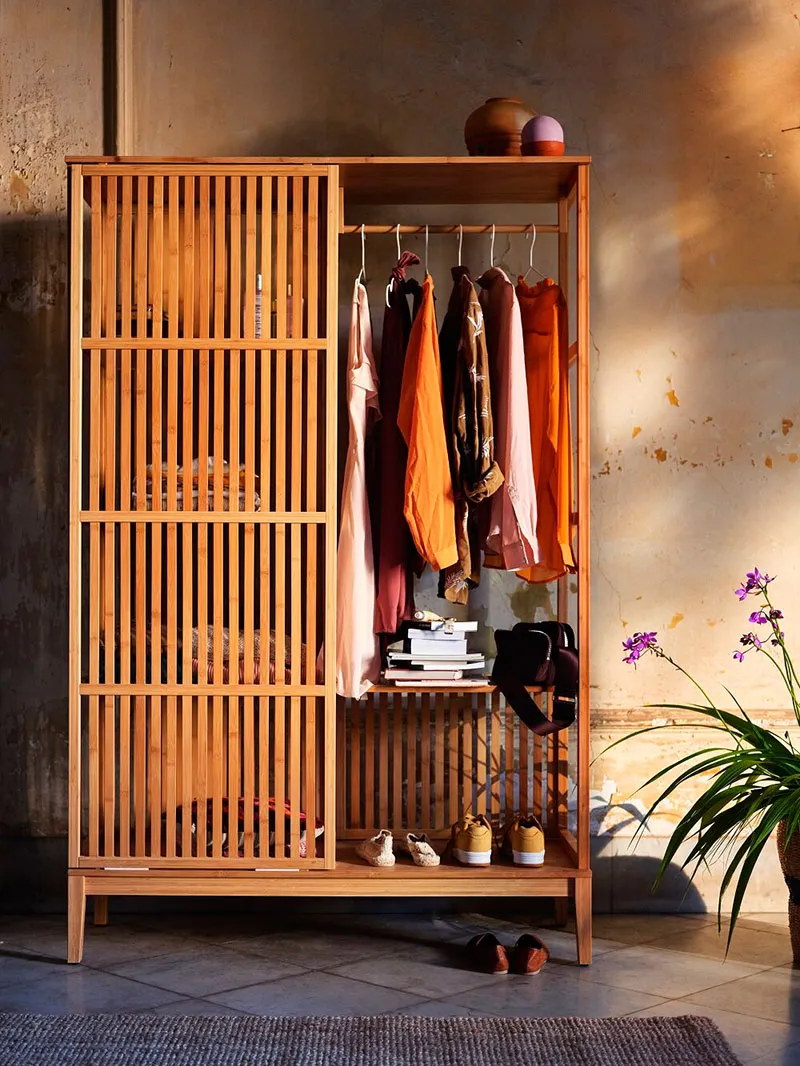 A modern wooden wardrobe with open shelves, clothing hung, and shoes on the bottom shelf.