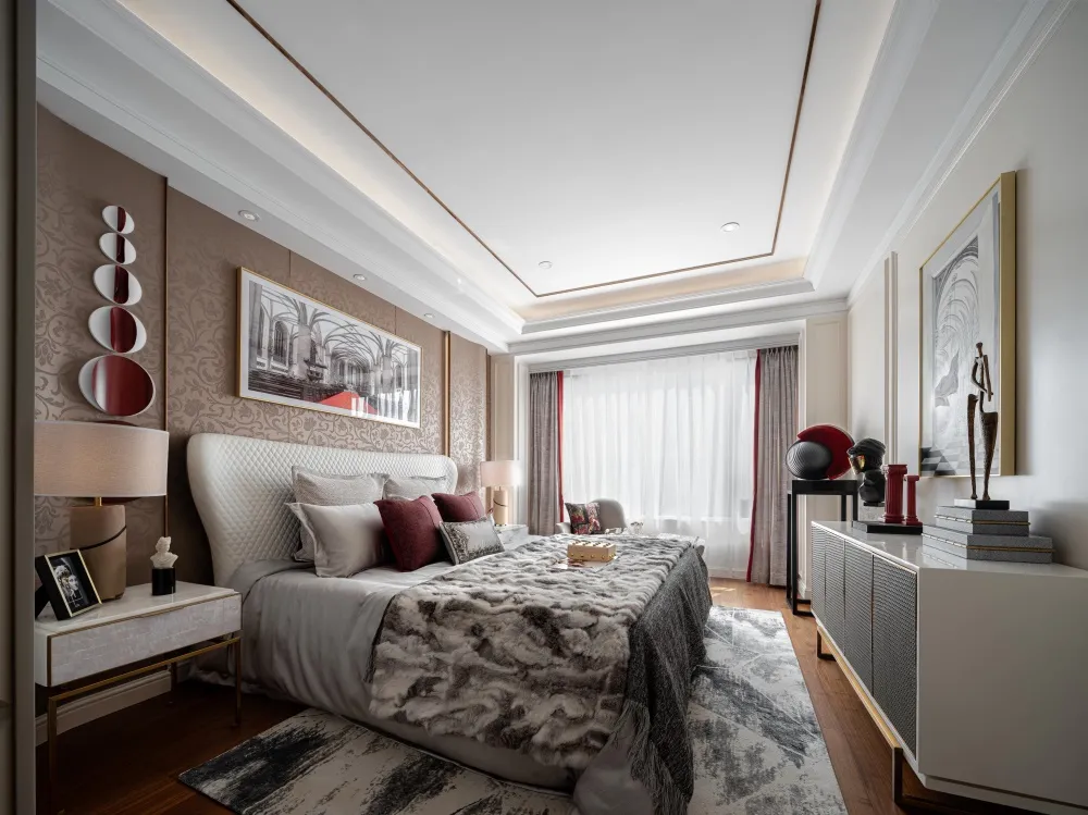 A modern bedroom with a large bed, white and red pillows, and a fur blanket, surrounded by framed artwork, a white dresser, a