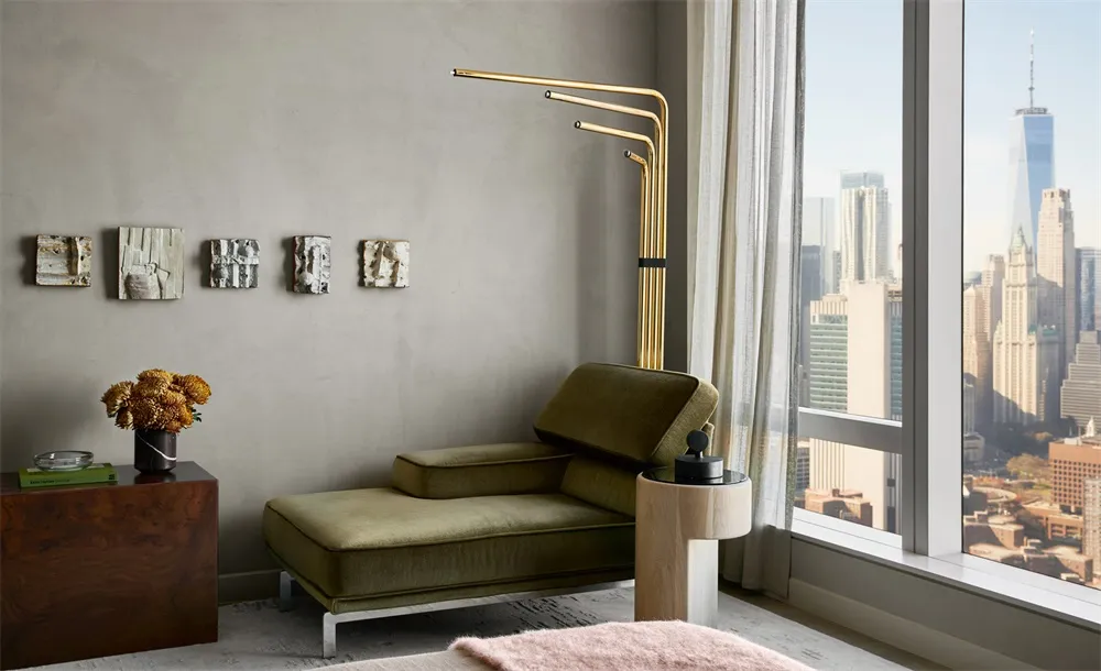 Minimalist living room with a green velvet couch, white curtains, and a cityscape view from a large window.