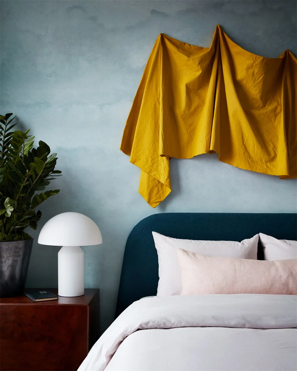A minimalist bedroom with a yellow duvet, white bedding, and a wooden side table.
