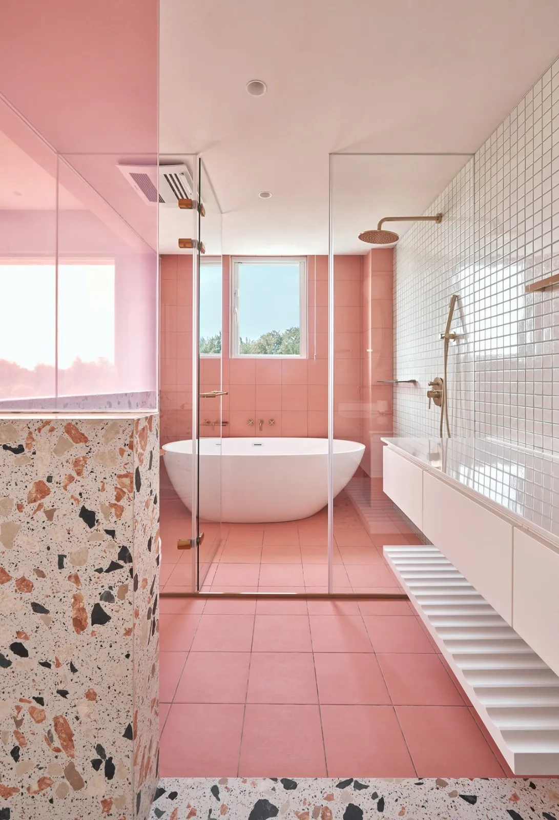 Modern minimalist bathroom with pink tiles, freestanding bathtub, and white floating vanity.
