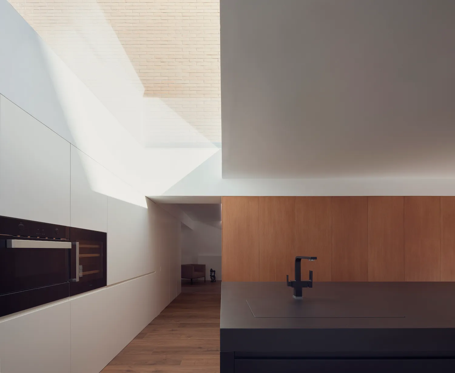 Modern kitchen space featuring white wooden cabinets on a matte black countertop, with natural light streaming through a larg