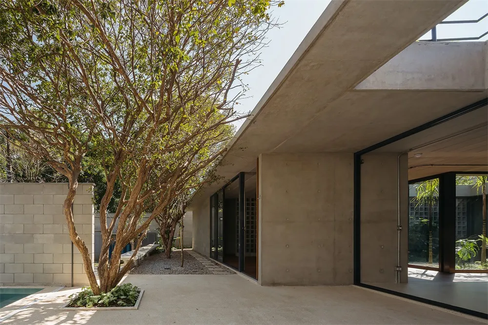 A contemporary house with a concrete exterior featuring a large overhanging roof and glass doors connecting to an outdoor spa