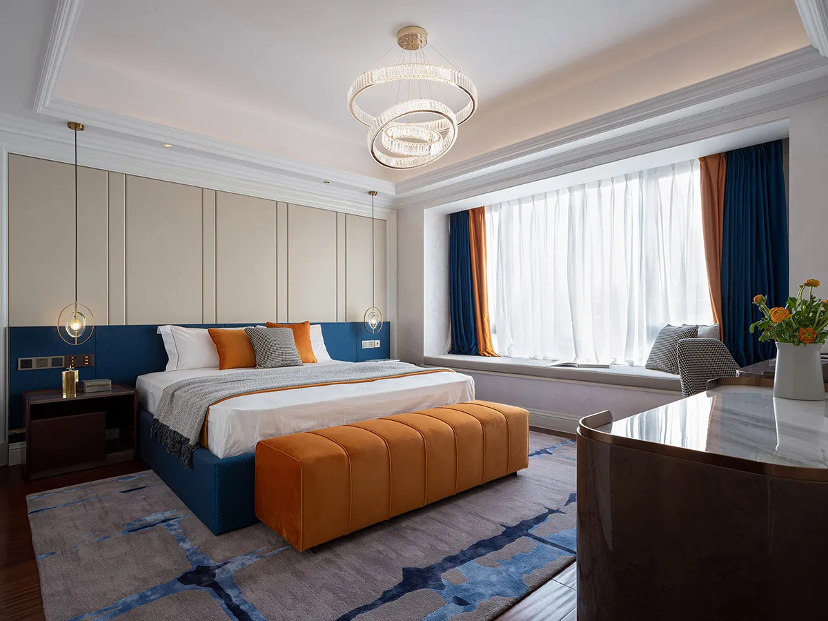 Contemporary bedroom design featuring a large bed, orange headboard, blue and orange curtains, and a circular chandelier.