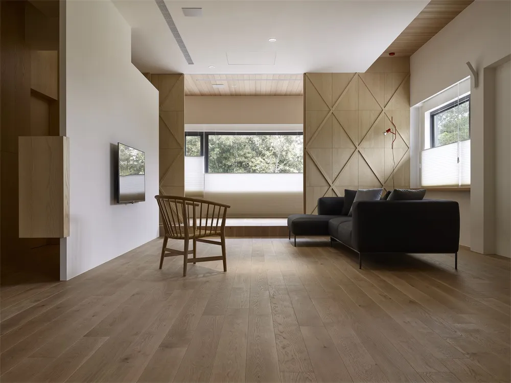 Modern interior space featuring wood flooring, minimalistic furniture, and large windows overlooking a natural landscape.