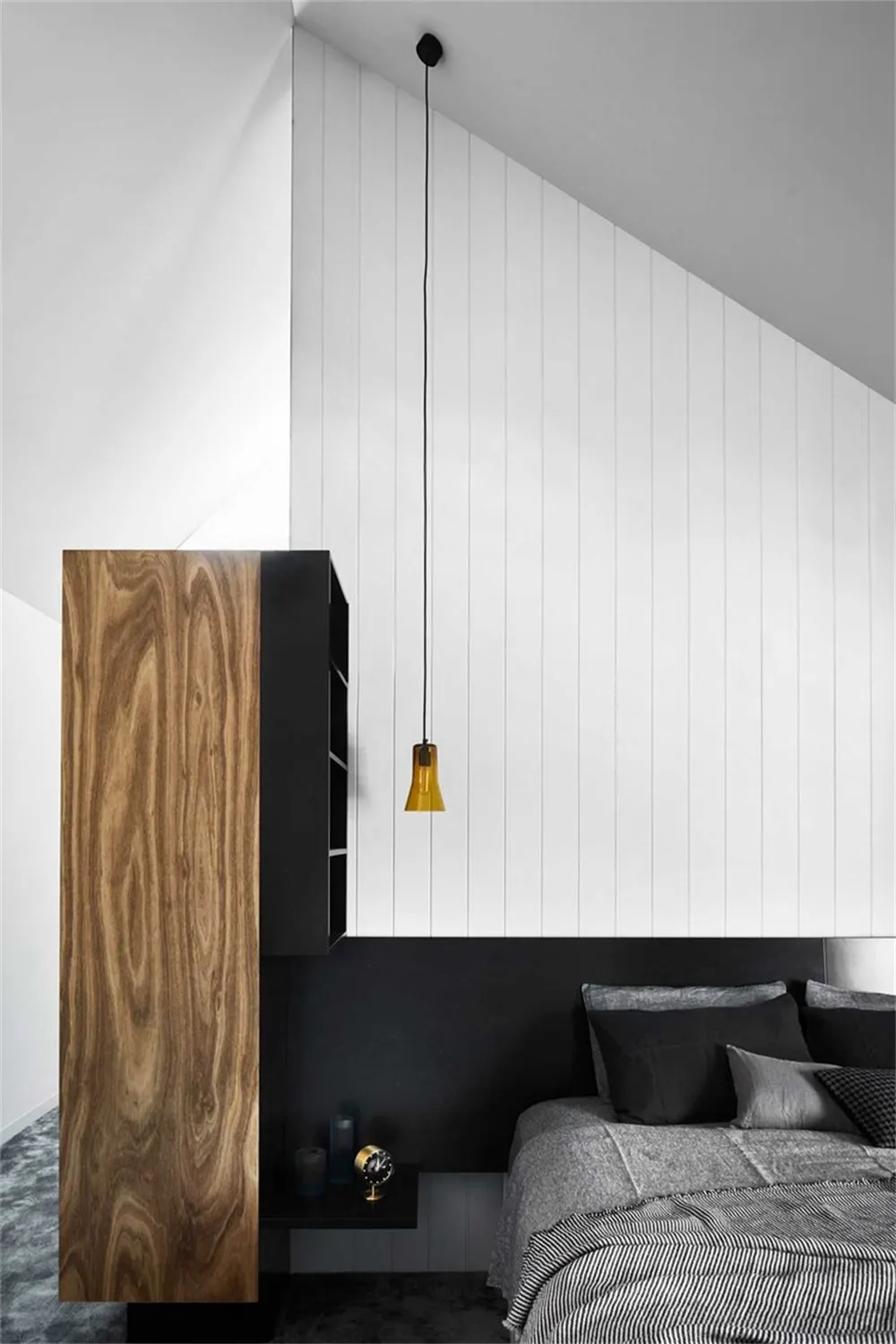 A modern minimalist bedroom with a wooden headboard and pendant light hanging from the ceiling.
