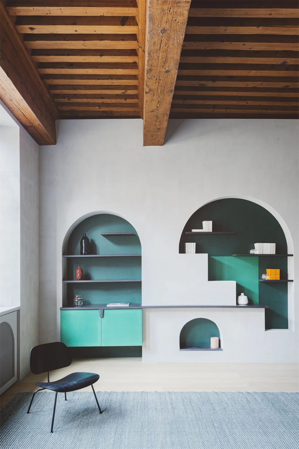 A minimalist living room with white walls, green shelves, and concrete and wooden furniture.