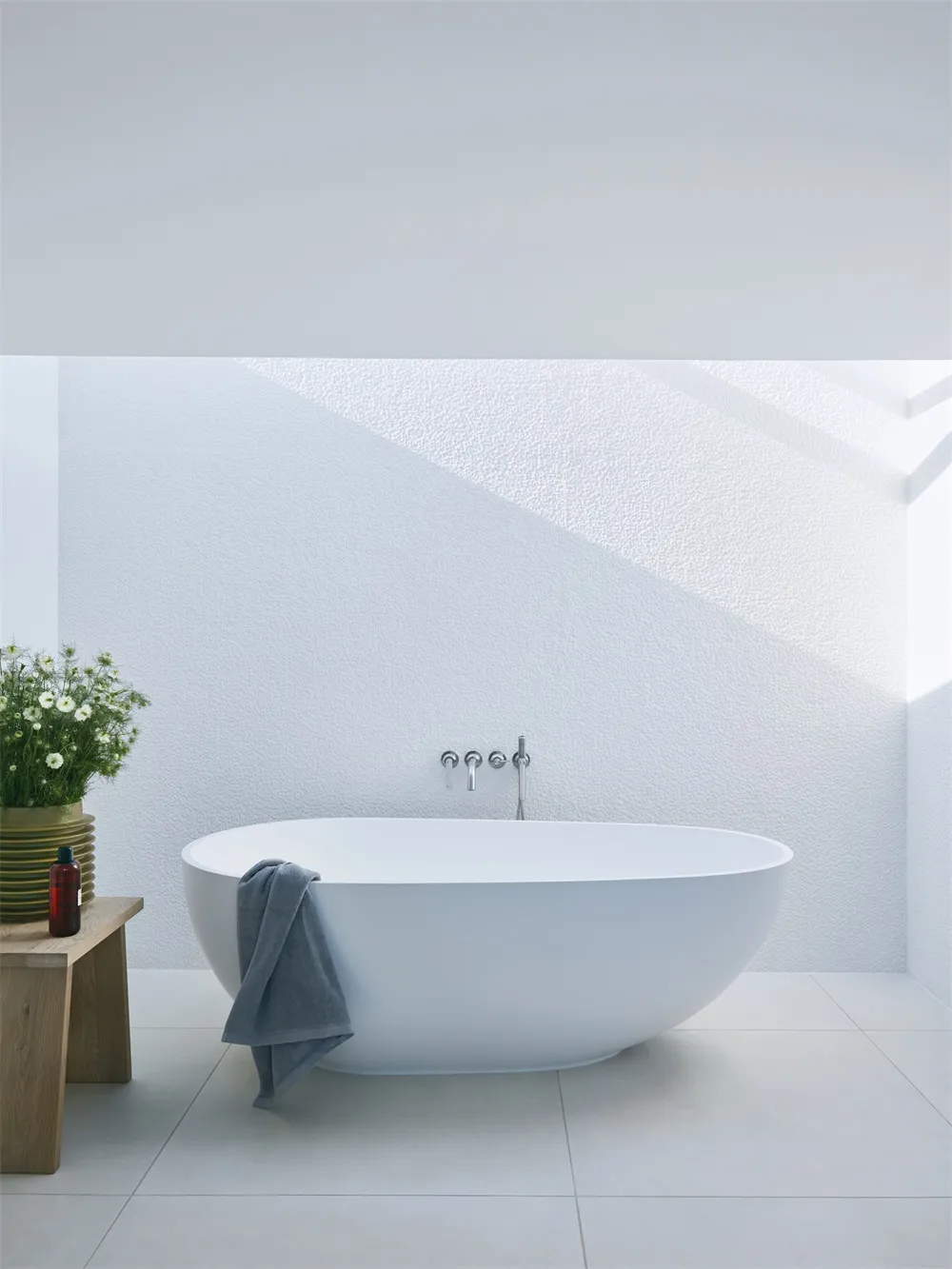 A minimalist white bathroom with a concrete bathtub and a bench with flowers and a towel.