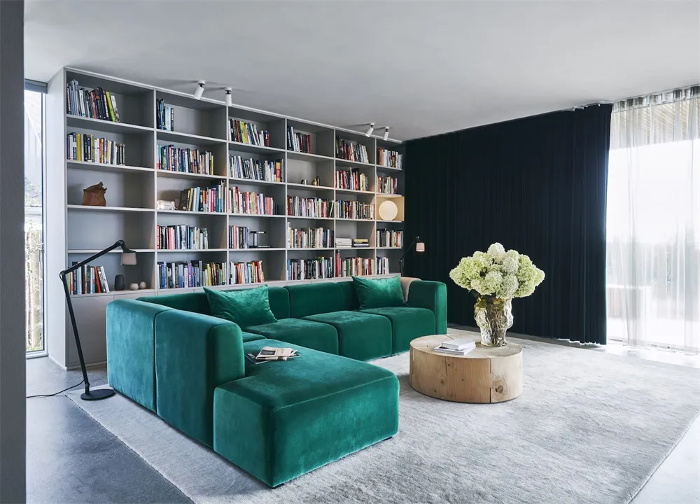 Modern living room featuring plush green velvet couches and a round wooden coffee table adorned with a white flower arrangeme