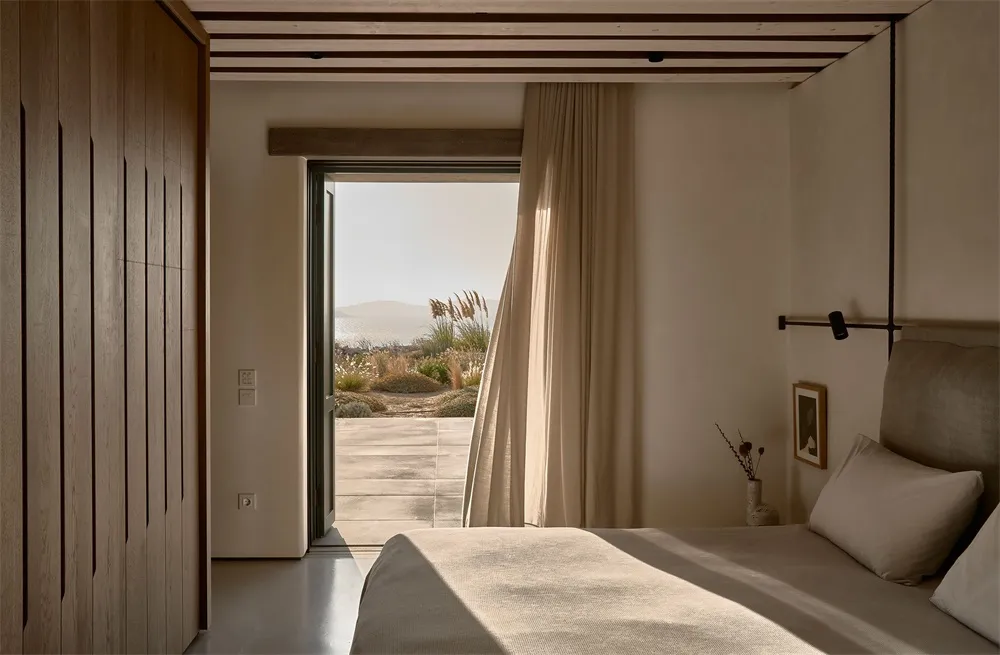 A minimalist bedroom with a bed covered in cotton sheets, overlooking a desert landscape.