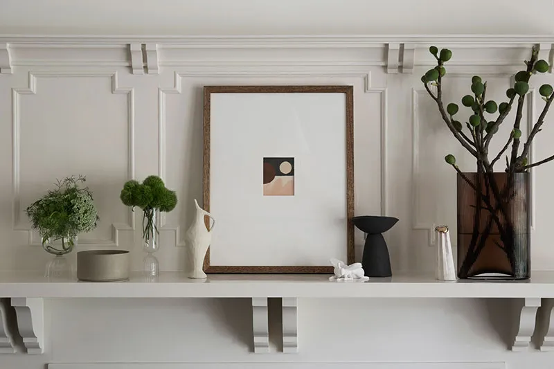 A minimalist shelf featuring a frame with a geometric abstract artwork, a small green plant, and various modern decorative it