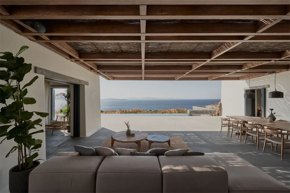 Modern living room with concrete flooring, wood accents, and glass windows overlooking the sea.
