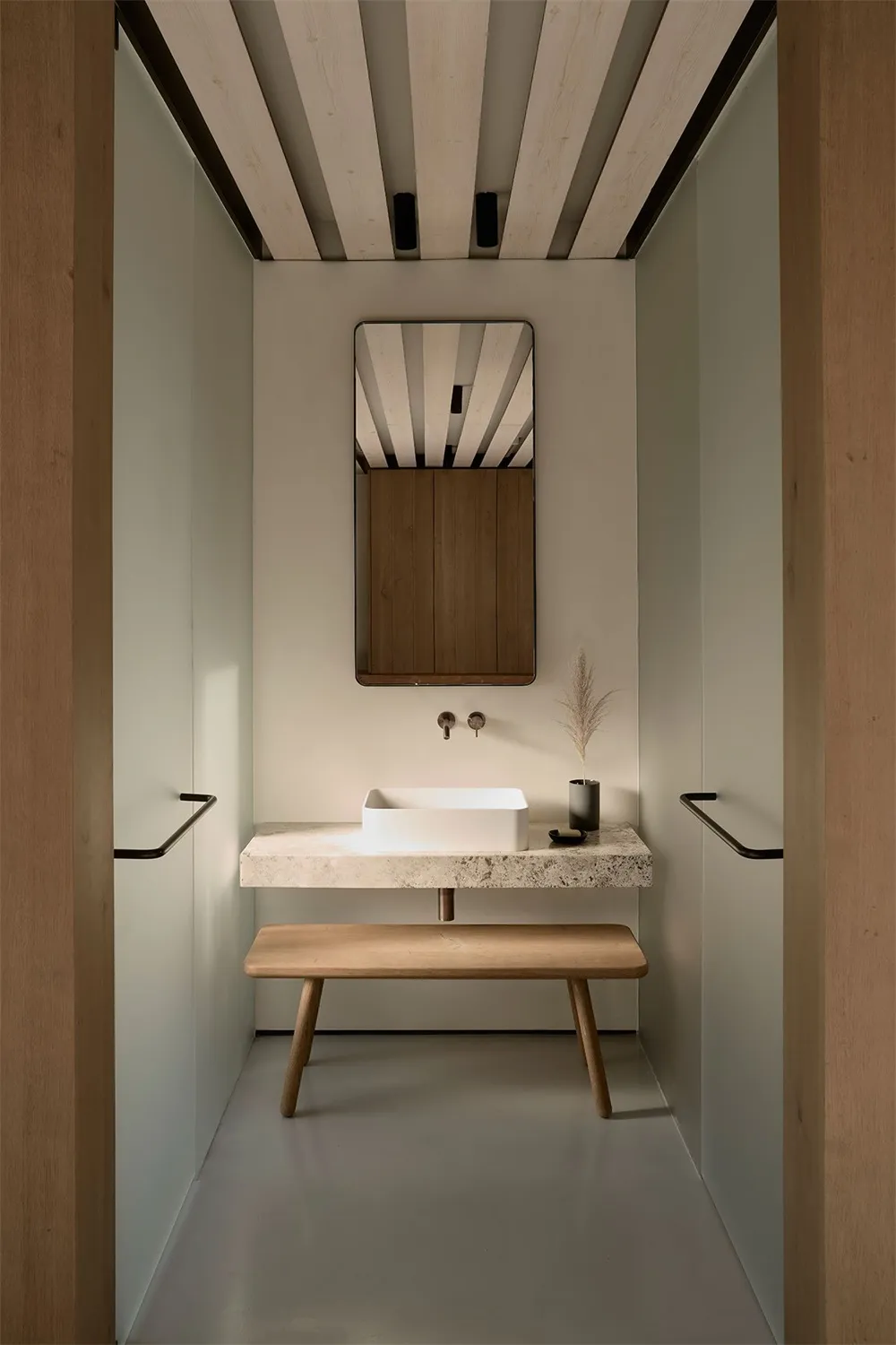 A modern minimalist bathroom featuring a concrete countertop and bench, with a sleek white sink and minimalist mirror.