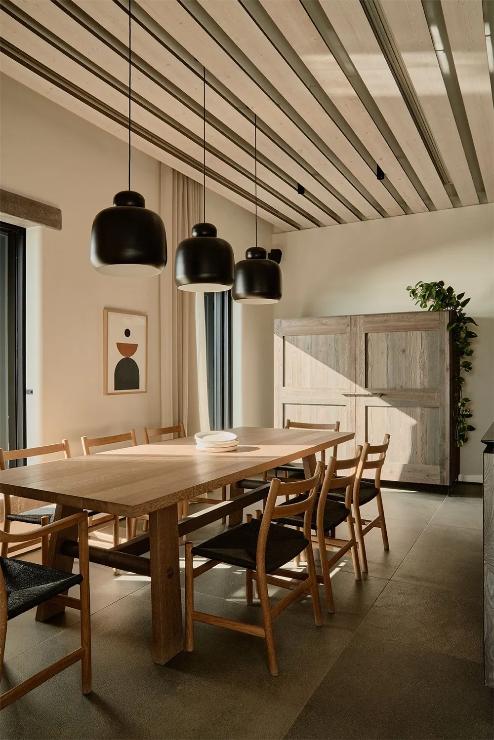A modern minimalist dining room featuring a wooden table and chairs, with a wooden ceiling and pendant lights
