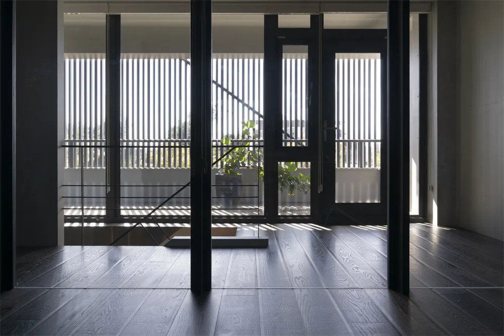 Modern living room featuring hardwood flooring and large windows with vertical blinds.