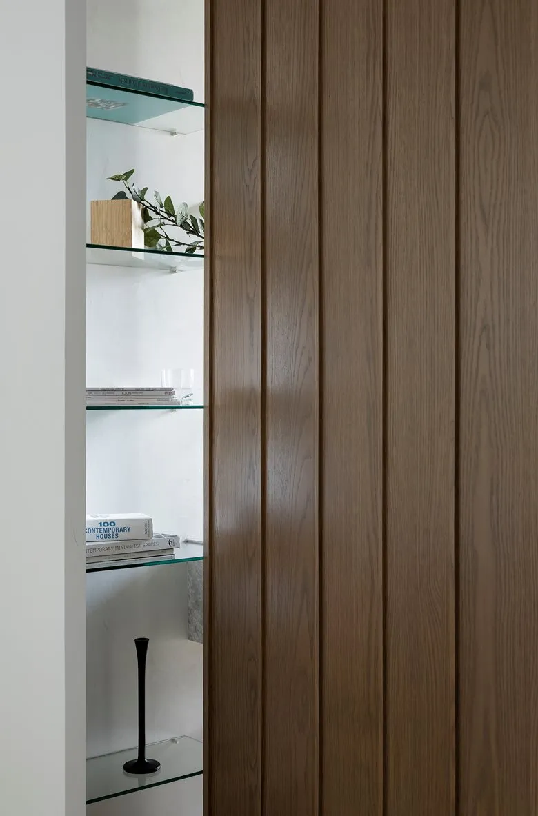Minimalist interior design featuring glass and wooden shelves with books and a plant.