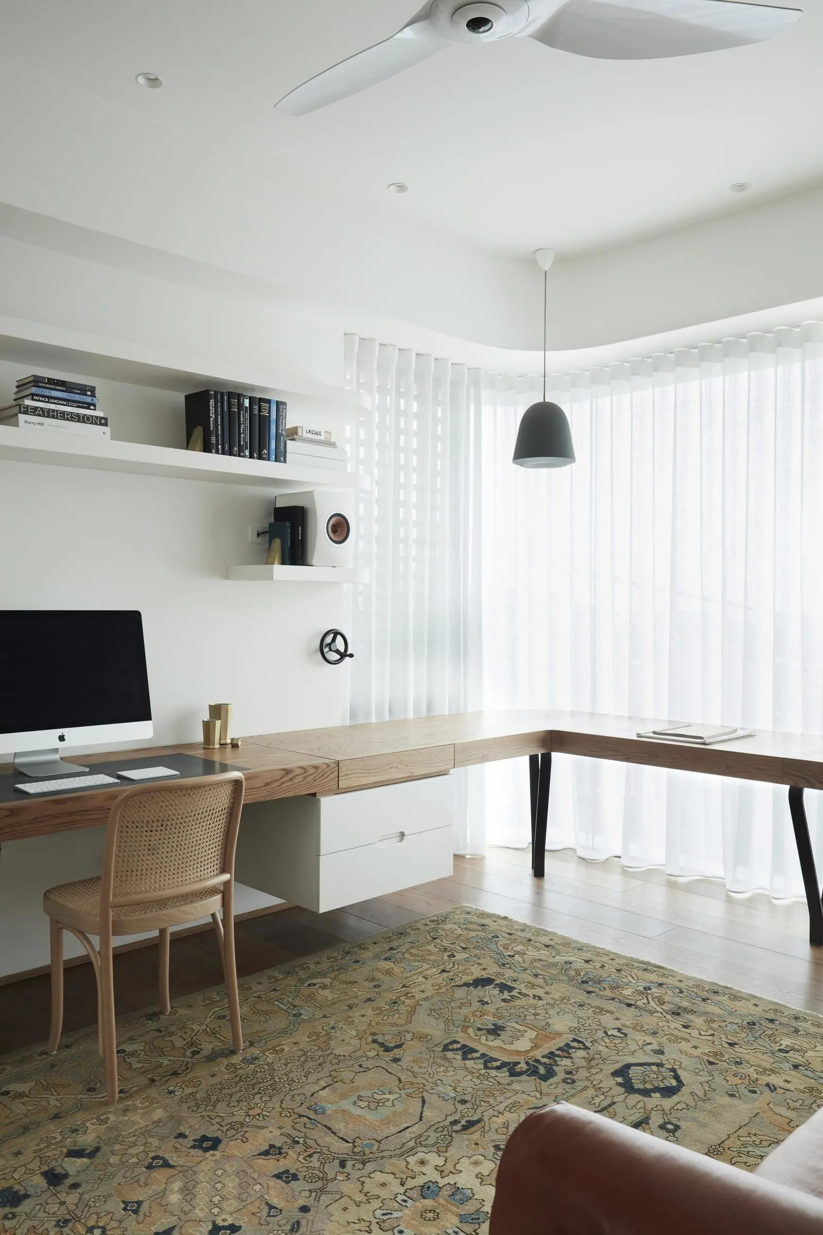 A minimalist home office featuring a wooden desk, leather armchair, and patterned rug.