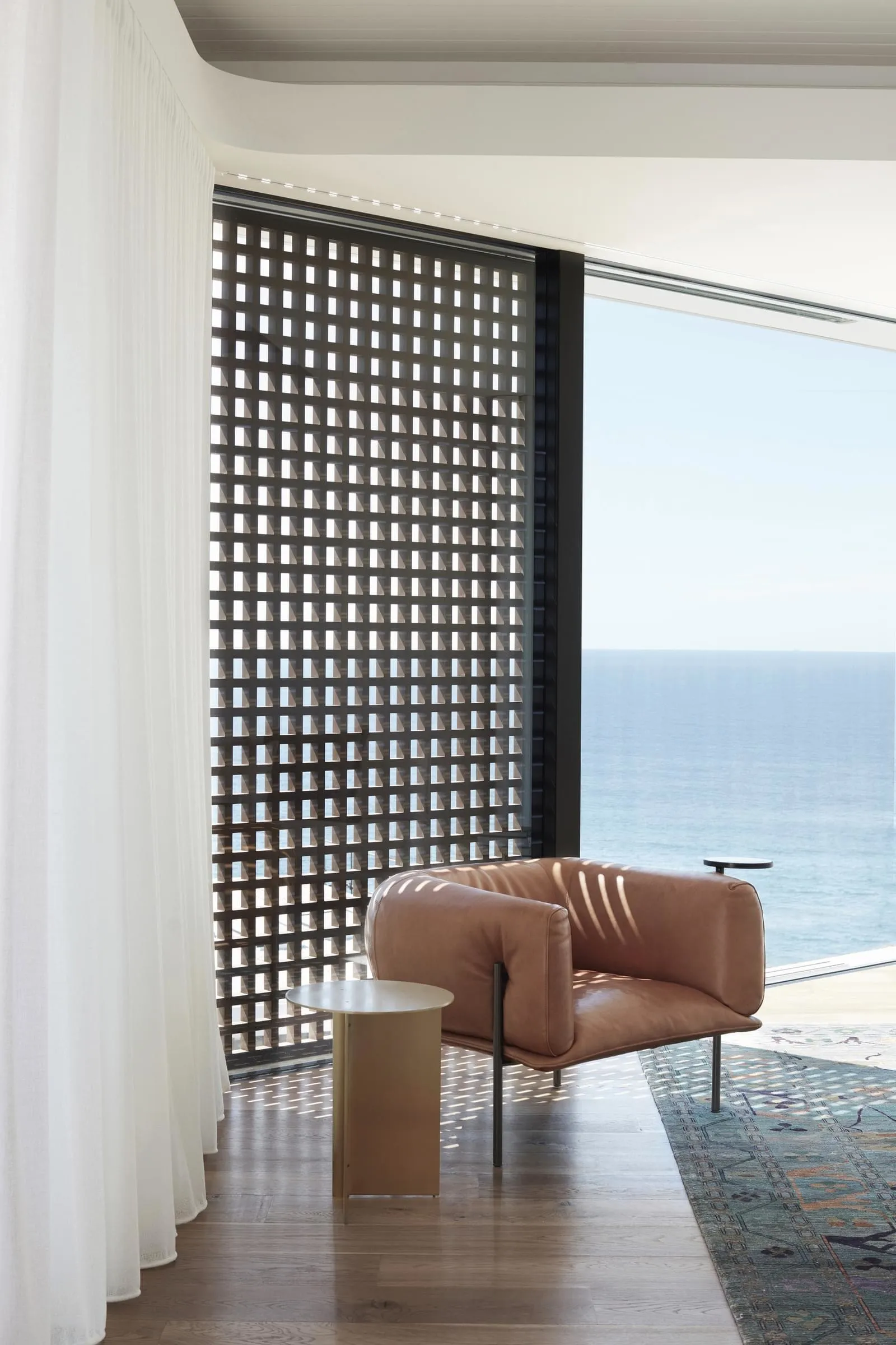 A modern residential interior featuring a sleek, brown leather armchair, a wooden side table, and a large window with ocean v