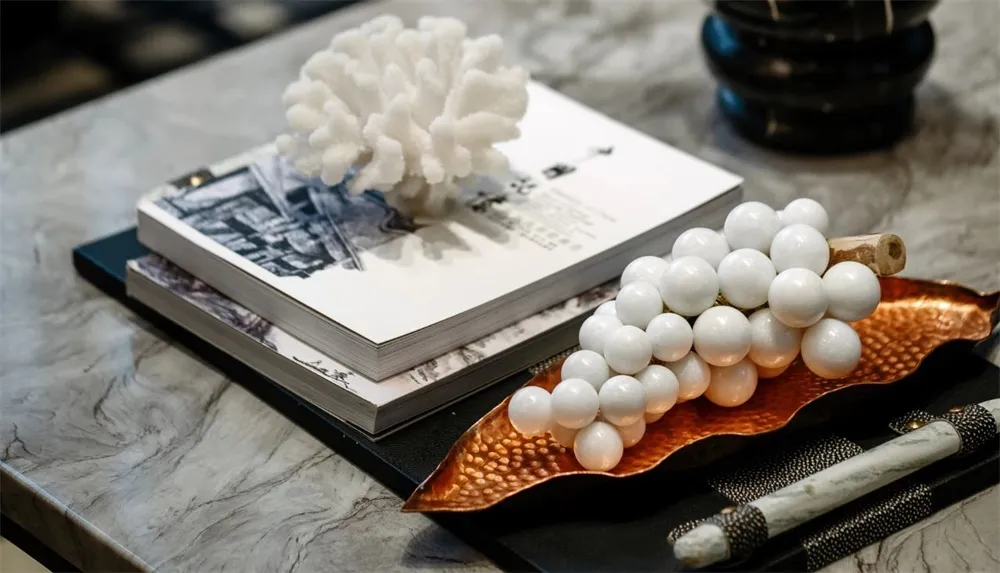 Decorative white spheres arranged on a metal plate, placed on a marble table with books and coral decor.