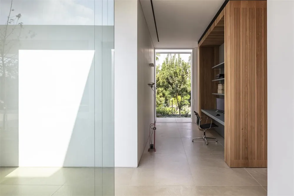 A minimalist office interior with concrete walls and floor, featuring a desk and chair, and large windows with a view of gree
