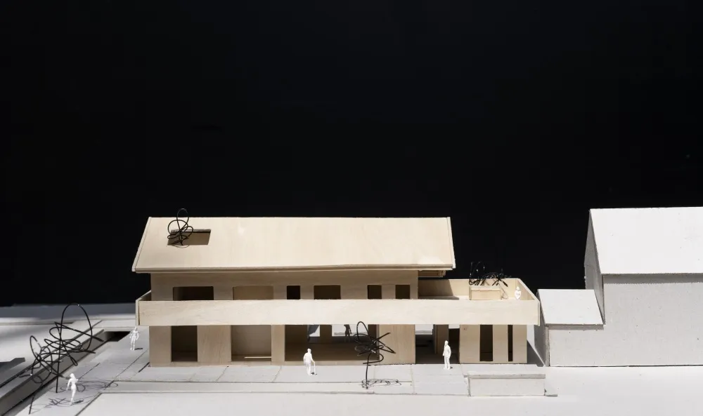 A wooden architectural model of a modern building with an open floor plan and outdoor seating.