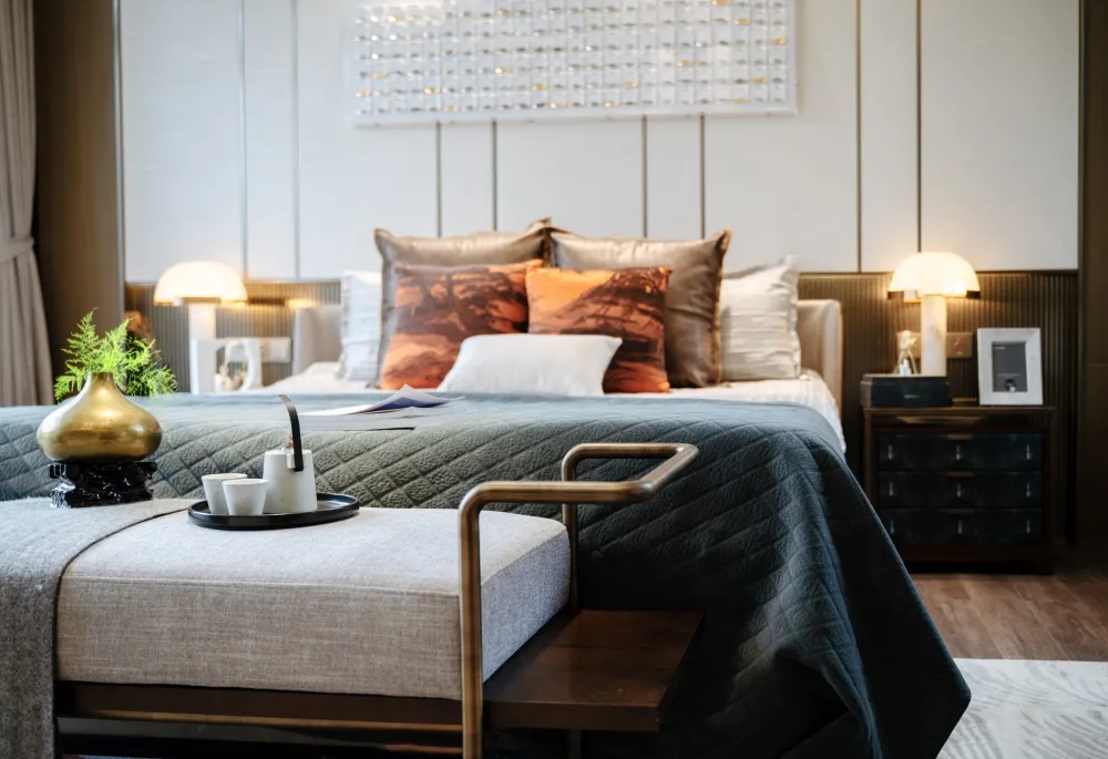 Modern bedroom with a bed featuring a quilted bedspread and metallic accents, surrounded by decorative pillows and a bedside