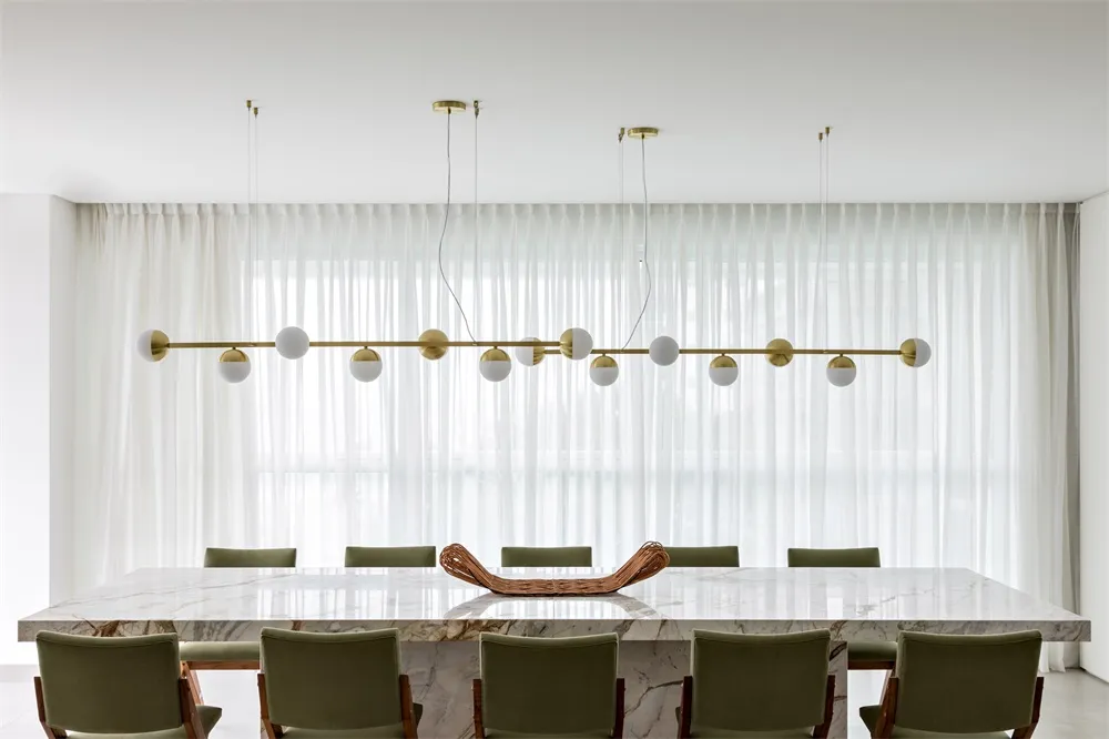 Modern dining room featuring a large table made of marble and a hanging light fixture with spherical bulbs.