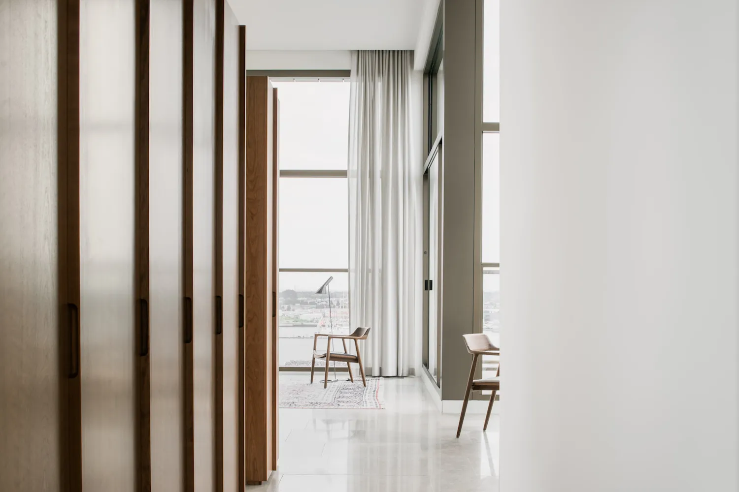 A modern interior white corridor with wooden doors and a view through a large window.