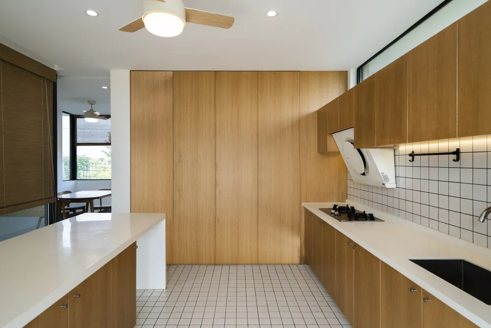 Modern kitchen interior with white countertops, wooden cabinetry, and tiled backsplash.